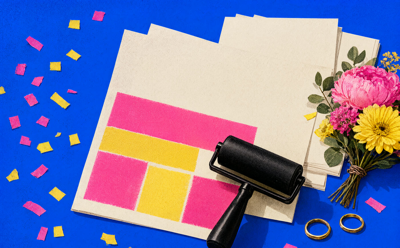 A cobalt print-shop table with a blank proof sheet, ink roller, wedding rings, flowers, and confetti.